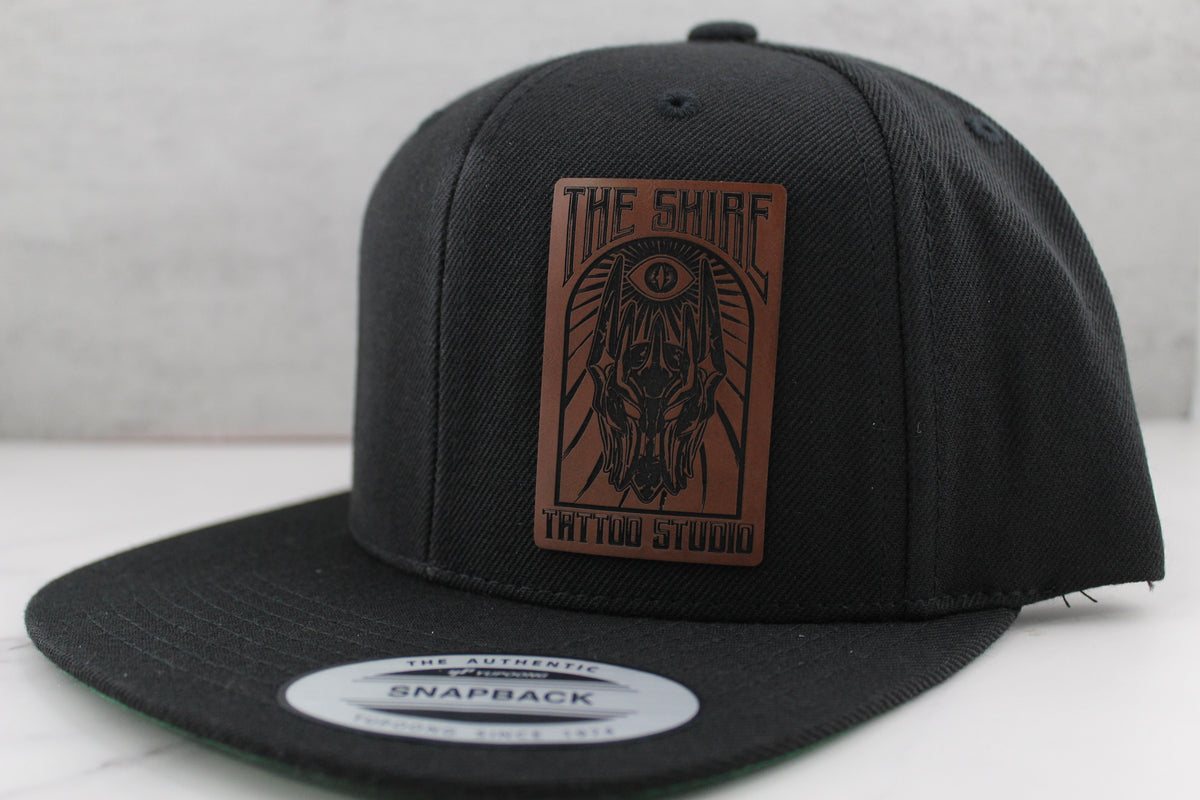 Black snapback cap with a leather patch on a white surface
