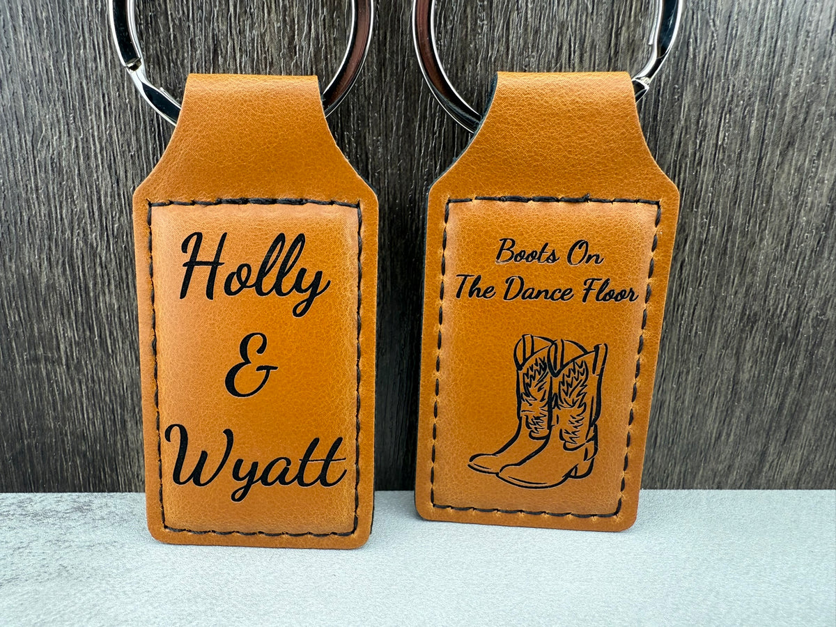 Two brown leather keychains with engraved text on a gray background