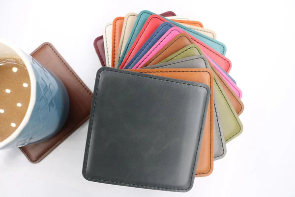 Square leatherette coasters in assorted colors displayed fan-style, shown next to a mug – Heritage Collection